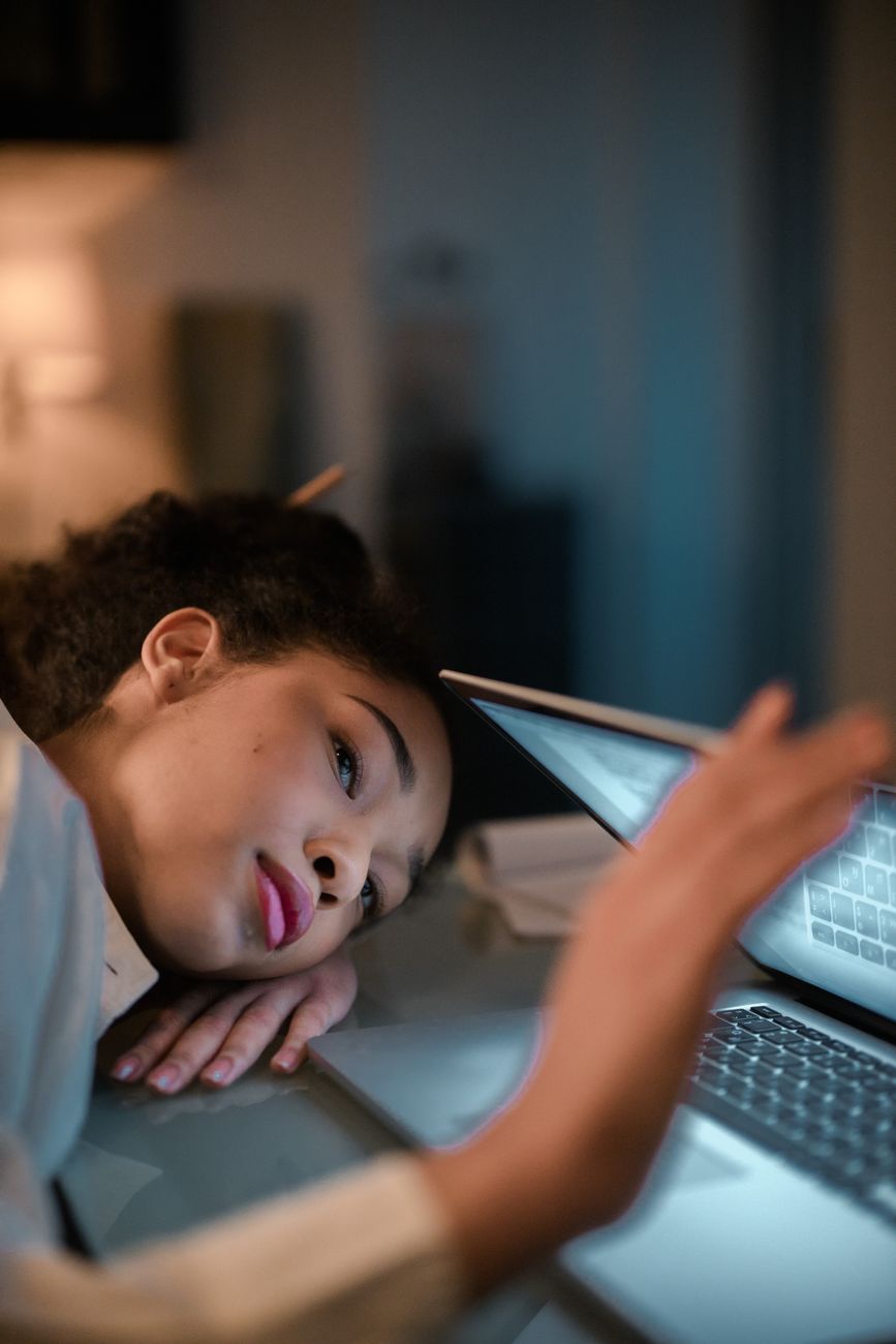 夜遅く自宅の机でノートパソコンの横に突っ伏して眠そうにしている人