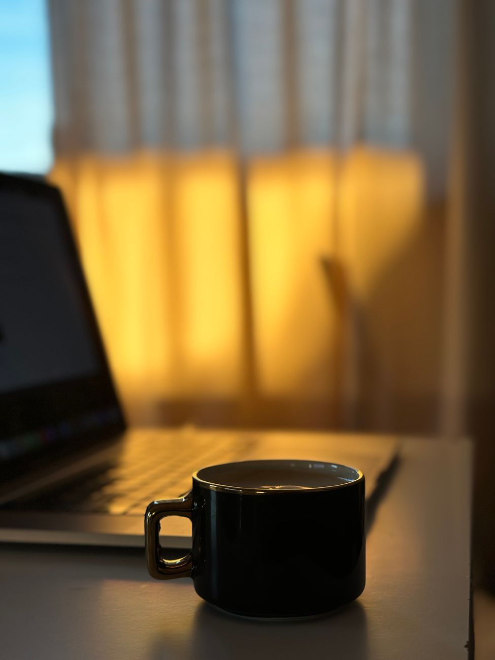 夕方の光が差し込む部屋でノートパソコンとコーヒーカップが置かれた静かな作業机